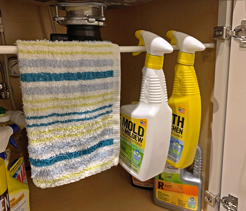 Spray bottles hanging from a tension bar rod under the sink