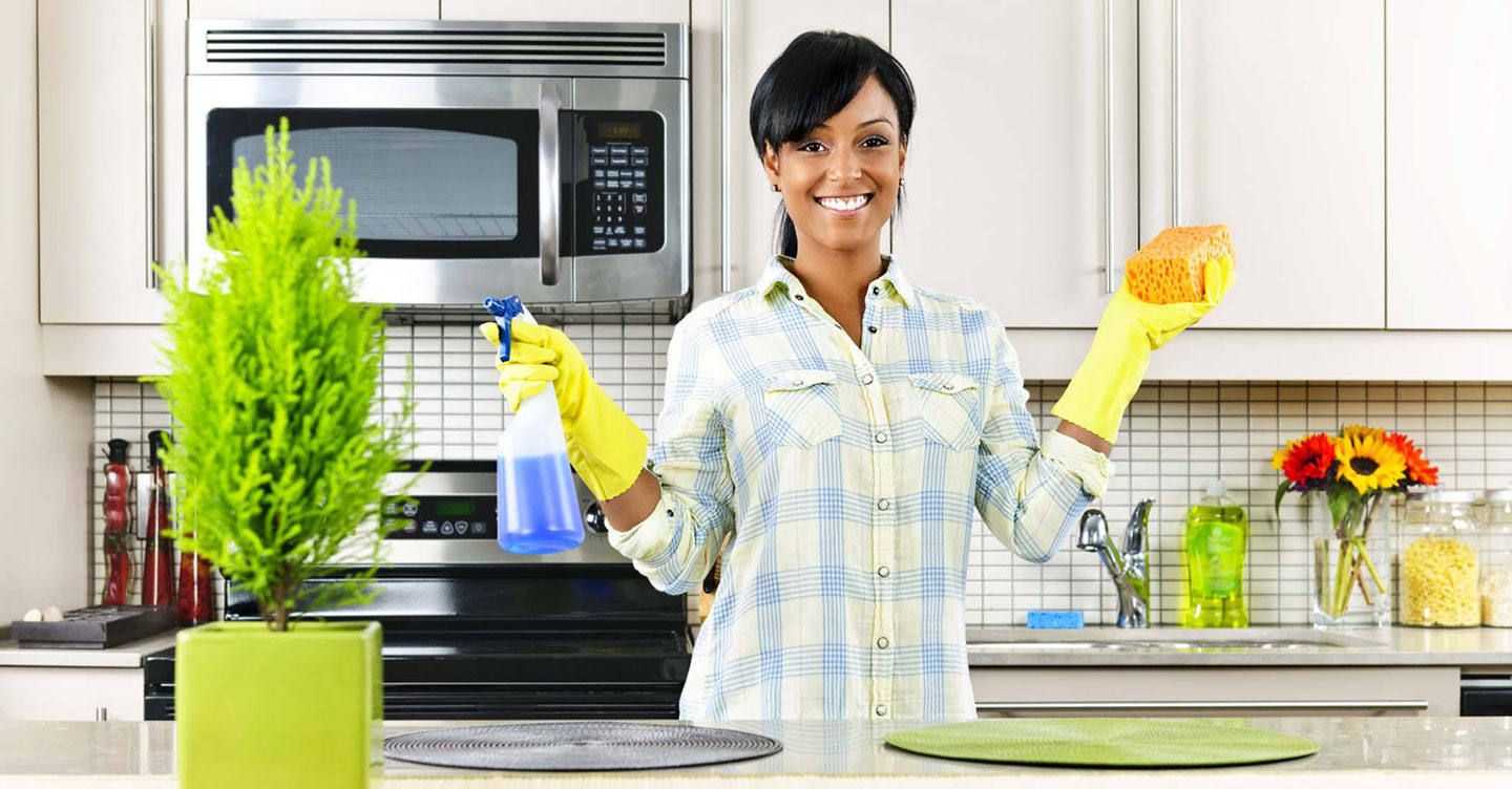 In her kitchen, a woman wearing gloves holds a sponge and spray bottle, ready to clean.