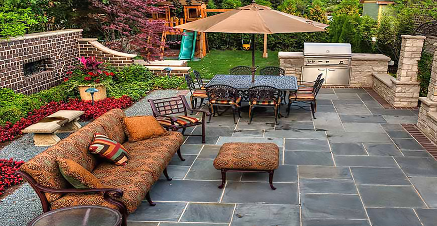 A lush yard with lots of plants featuring a swing set and patio full of furniture