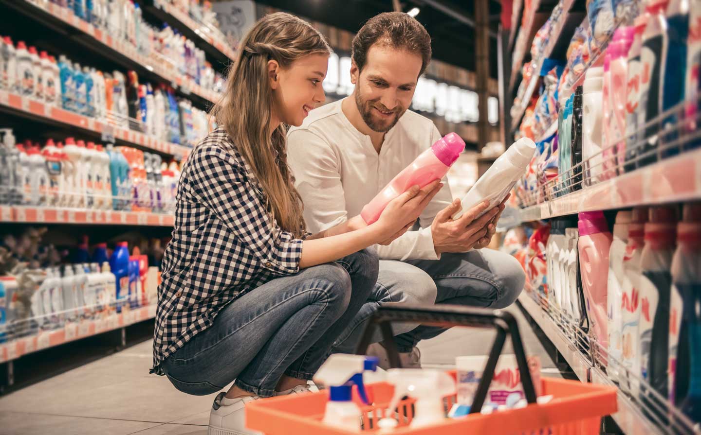 A man and woman crouch down at the store to inspect cleaning products on the shelves