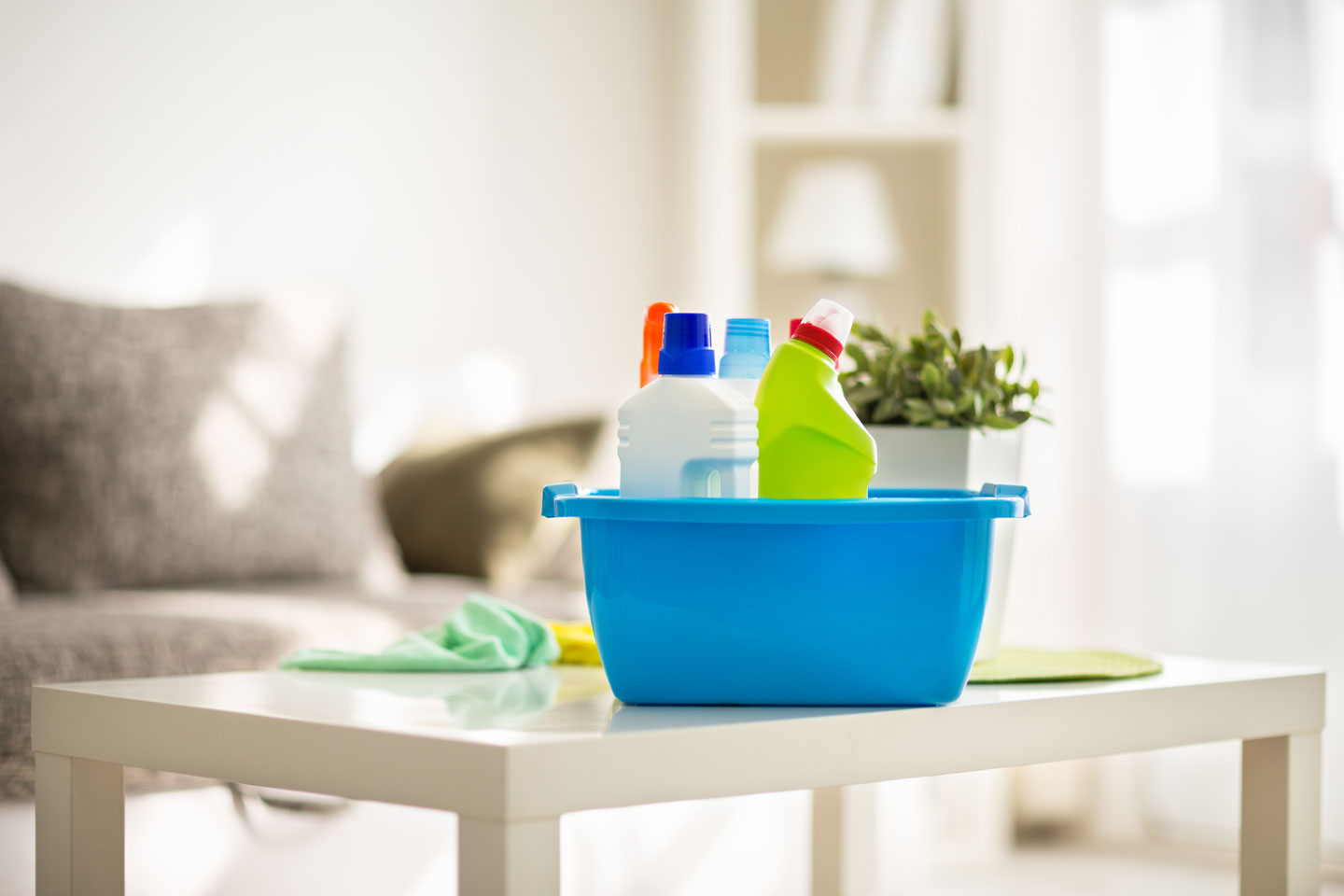 A blue plastic tub full of cleaning products sitting on a coffee table in the middle of a clean living room